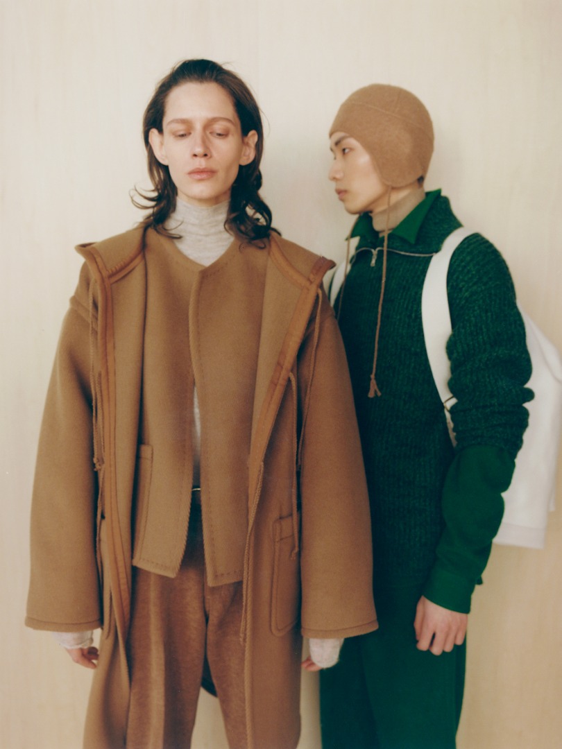 Ella wears Wool Herringbone Pile Hooded Coat in Brown, Wool Herringbone Pile Collarless Blouson in Brown. Yuta wears Wool Baby Alpaca Mix Rib Kint Zip Turtle in Top Mix Green, Brushed Baby Camel Melton Hand Sewn Cap in Camel