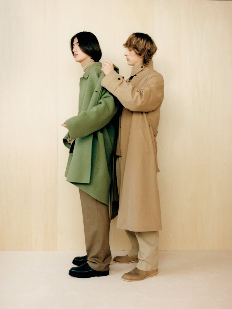 Kaan wears Velour Brushed Wool Melton Hand Sewn Hooded Coat in Sage Green. Josef wears Finx Hard Twist Gabardine Soutien Collar Coat in Beige Chambray