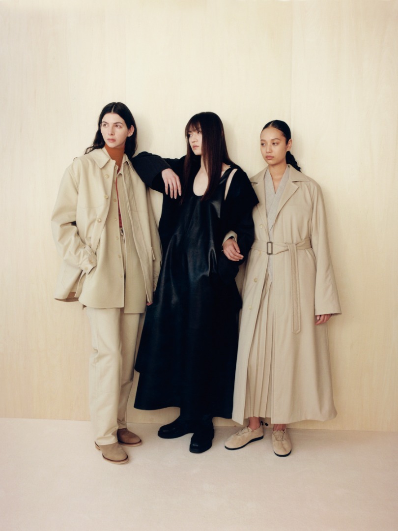 Tiger wears Cotton Oiled Canvas Liner Blouson in Light Beige. Miki wears Light Lamb Leather Dress in Black. Aria wears Super Fine Tropical Wool Chesterfield Padded Coat in Top Ivory Beige